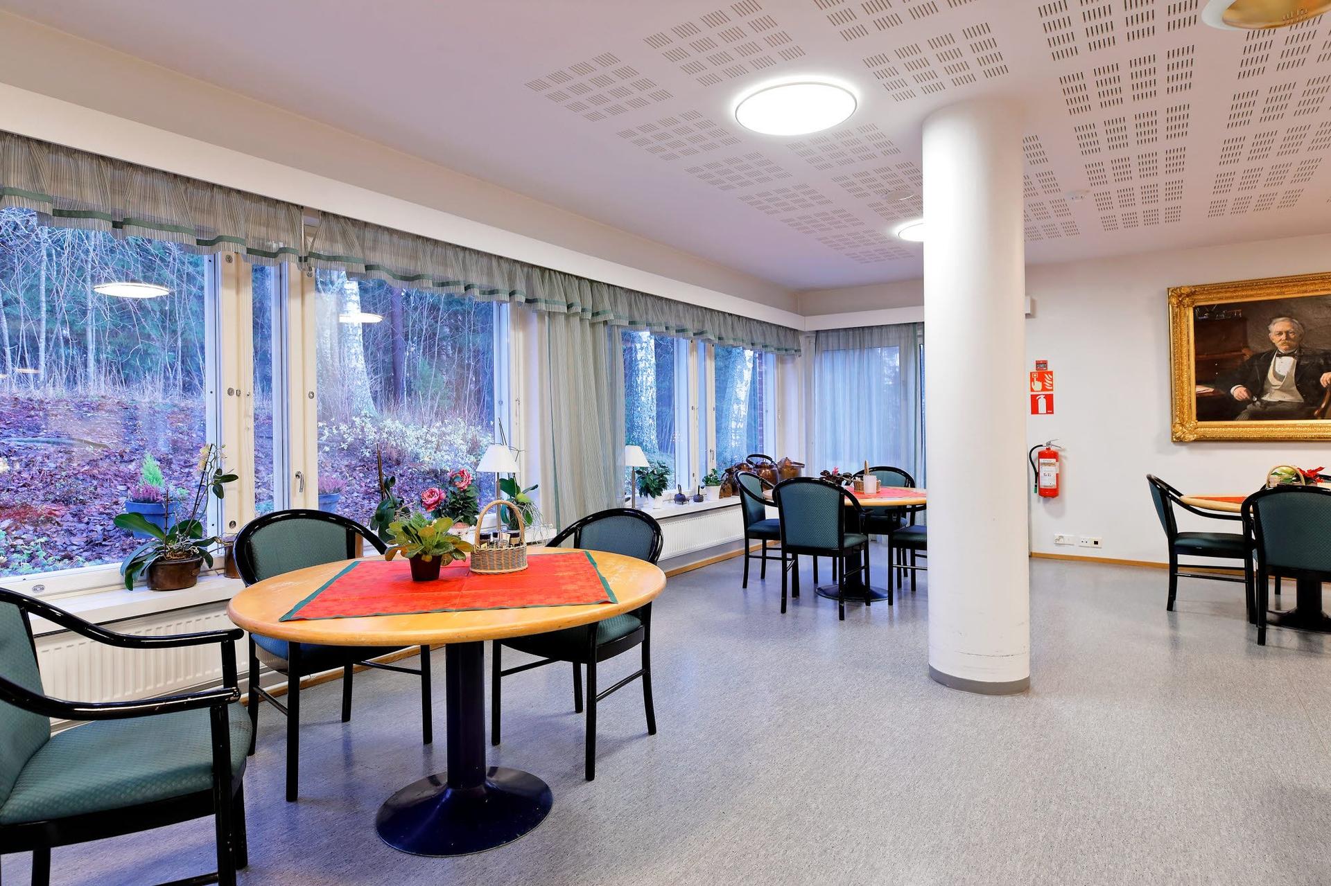 Ett ljust och rymligt matsalsutrymme på ett äldreboende, med stora fönster som vetter ut mot en skog